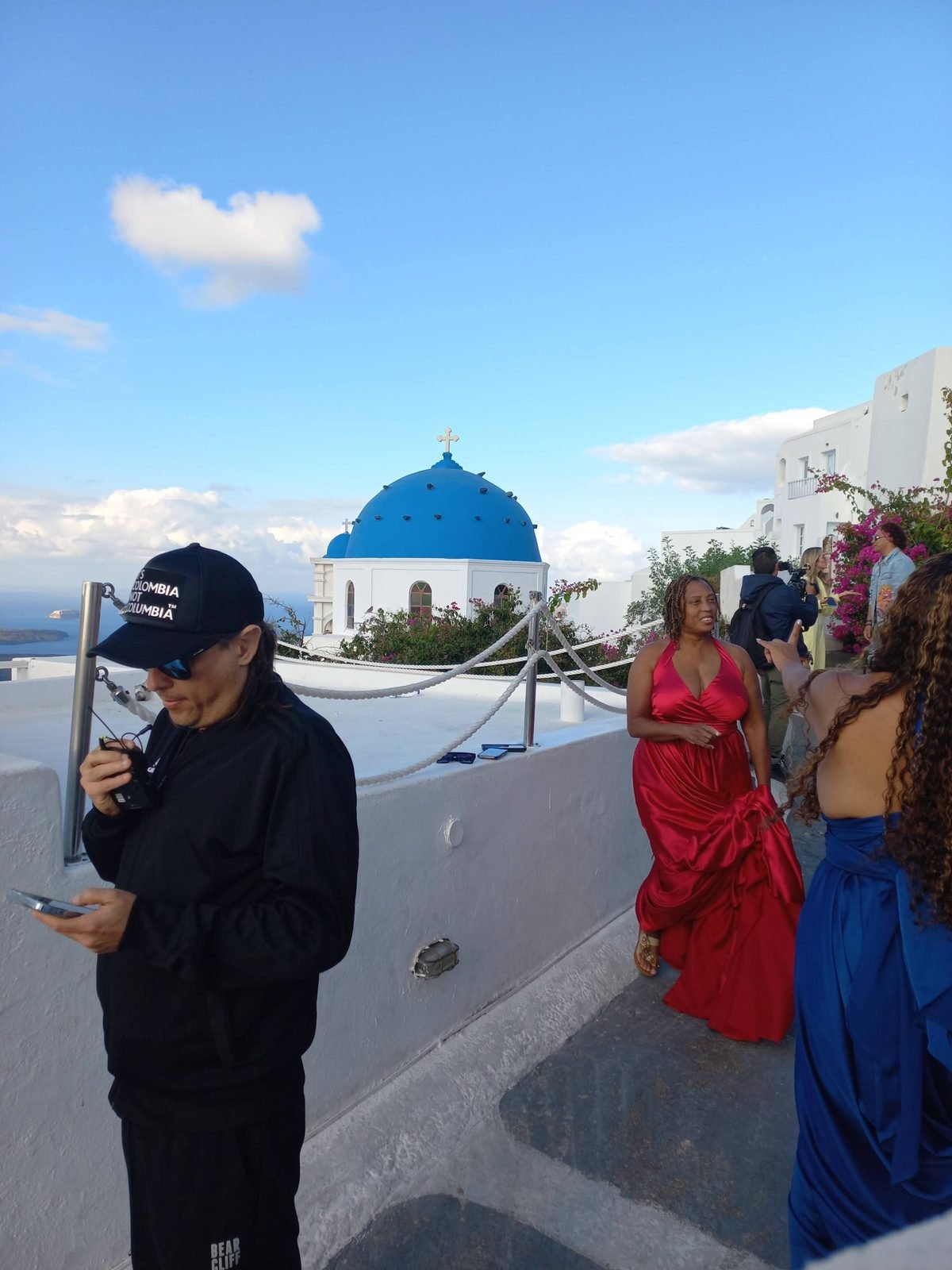 The crew and cast in red and blue gowns beside a blue-domed church on the caldera edge, Santorini, October 2022